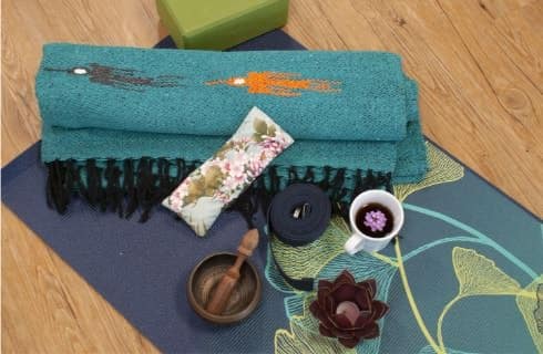 Blue and teal yoga mats with a bronze candle holder with tea light and white porcelain cup filled with tea