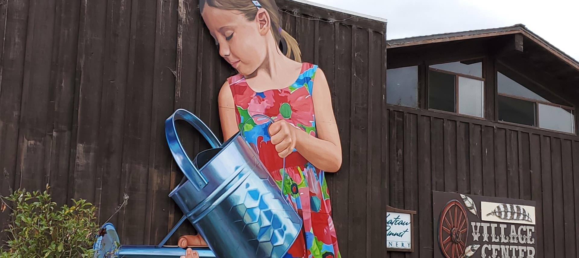 Dark wooden fence with a large picture of a child wearing a flower dress holding a metal watering can